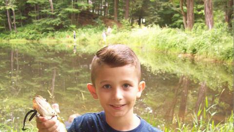 Camper holds up a fish they caught in front of the pond.