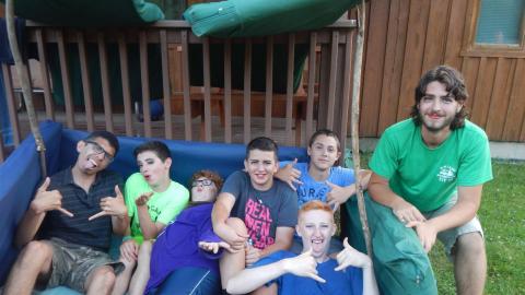 Cabin group seated together on mattresses with counselor. Youth have make-up on faces making hand gestures and blowing kisses at camera.