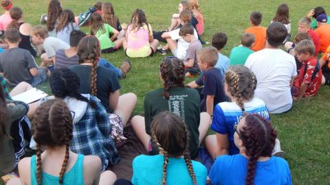 Group of youth with hair braided in the same style sit facing away from the camera.