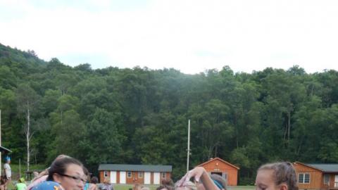 Large group of youth around a table grimacing with hands in messy tins of slime.