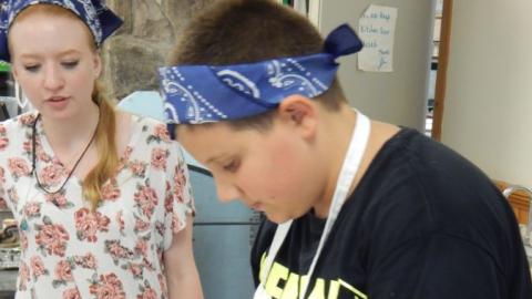 Youth opens a hard boiled egg over a bowl as a counselor looks on.