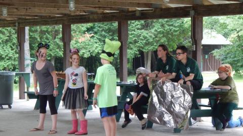 Campers in a play. One in a goofy hat. Two others wearing minnie mouse ears.