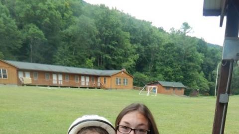 Counselor poses with camper dressed in sheet with white painted face in bike helmet and sunglasses.