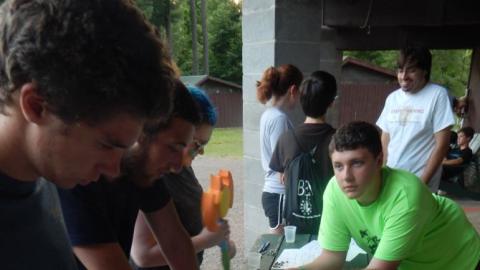 Youth around table on porch play 9 mans morris using rocks on paper boards.