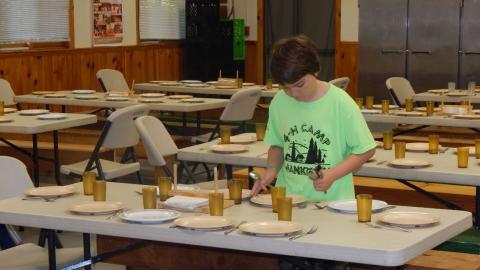 Youth sets spoons on a table they are preparing before a meal.