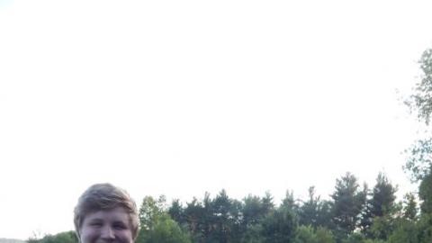 Counselor and campers smile at camera near picnic table containing hammer and board with single nail.