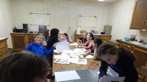 Youth seated around table looking at old camp newspapers and talking to one another.