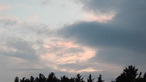 Blue, white, pink, sky over silhouette of trees in  distance.