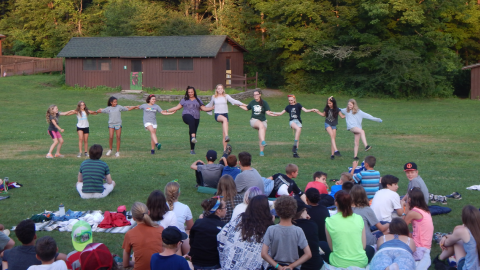 Cabin group standing in a kick-line with feet raised.