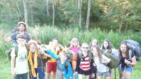 Group of campers with black handprints or marks across their faces posing with two counselors all wearing hiking backpacks.