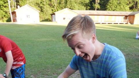 Teen yelling with hammer in hand at nail on board in front of them.