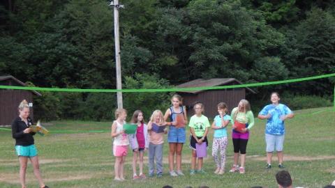 Cabin group in a line with folders as counselor to the side reads a story.