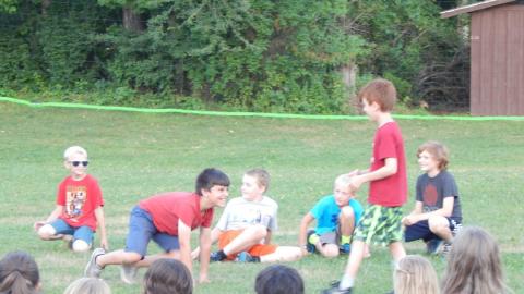Cabin group seated up front with one youth crawling like a bear toward another youth standing before him.
