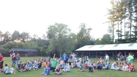 Campwide group sitting on lawn cheering toward the camera.