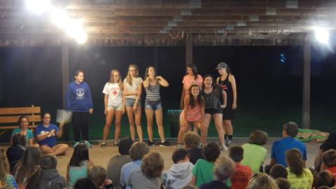 Cabin group standing together in front of rest of camp seated in the rec hall.