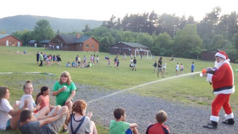 Counselor dressed as Santa sprays seated platoon group with water gun.