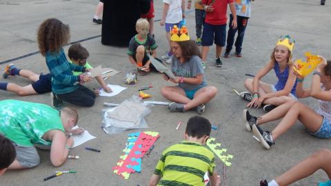 Campers seated on basketball court making paper crowns.