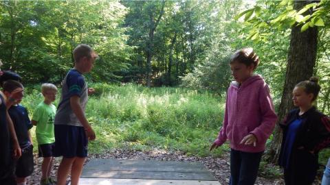 Campers balance on a wooden platform in ropes course area.