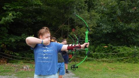 Youth on the shooting line stand with bows drawn.