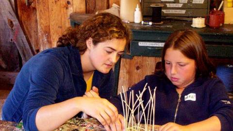 a youth sitting with the Craft Director who assists her with a basket weaving project one-on-one