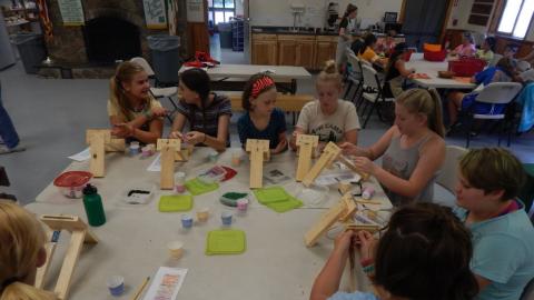 Youth seated around a table stringing beads onto wooden looms.