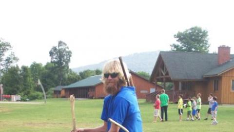 Counselor holding walking sticks in both hands with additional sticks in his belt loops and shirt.