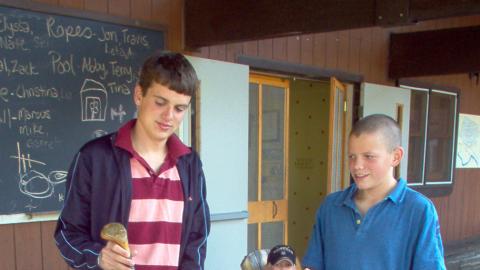 Three youth waiting on the dining hall porch with a set of golf clubs while they wait to be picked up by the bus to go to the golf course.
