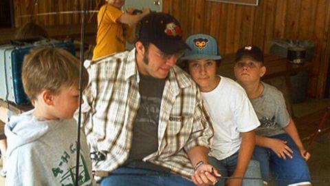 Four youth holding fishing poles as the class counselor readies one before the class heads out to fish.