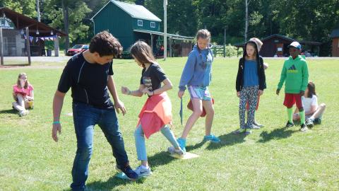 Class group stepping on rubber mats one at a time in a line across the field.