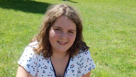 Camper holding tongs as a burger cooks over a coffee can on tin foil outside.