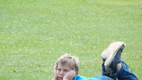 Youth laying in field with head in hands and feet up.
