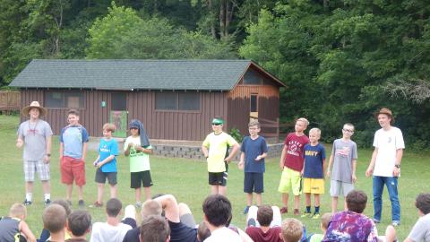 Cabin group in a line before campers seated in audience.
