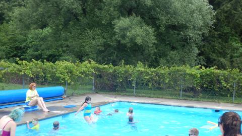Pool Director and lifeguards watch over a group of swimming day campers. One is in a life jacket.
