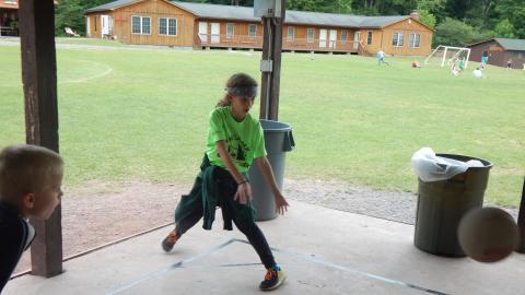 Camper in serving square with hands outstretched toward a rubber ball.