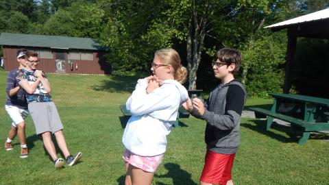 Campers in pairs complete trust falls with hands locked in front of them as their partner catches them.