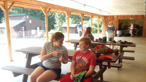 Two youth sit on picnic table talking.