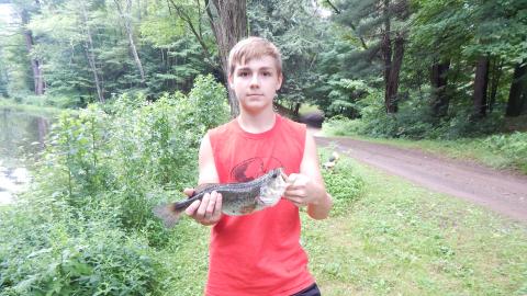 Camper holds a fish they caught next to the pond.