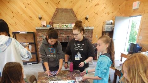 Campers around a table with colorful marbles shaving cream paper in front of them.