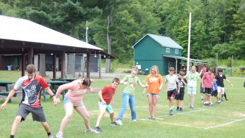 Youth step onto rubber mats spread across a field in a line with one foot between two mats so as not to leave any mat unoccupied.