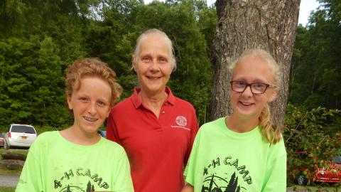 Two campers wearing camp t-shirts pose with CCE educator holding bowls of snacks they have prepared in chefs club.
