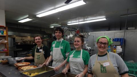 Kitchen staff standing in front of hot pans ready to serve and smiling at the camera.