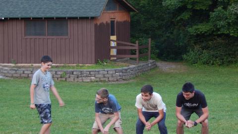 Three campers crouch down in a line as another walks up to them.