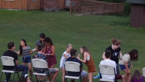 Counselors seated in folding chairs receive a make-over from another cabin group.