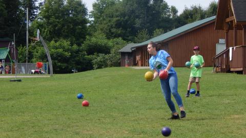 Youth holding two balls with many more scattered on the ground during a game.