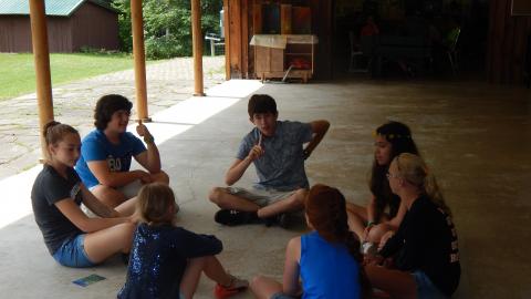 Youth seated in a circle on the floor talking.