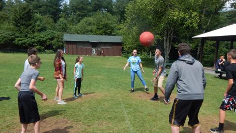 Youth playing ultimate 4square outside rec hall in teams of two.