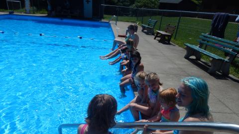 Youth seated on the pool deck with toes in the water.