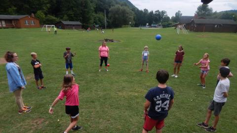 Youth standing in a circle in the field with a ball in the air.