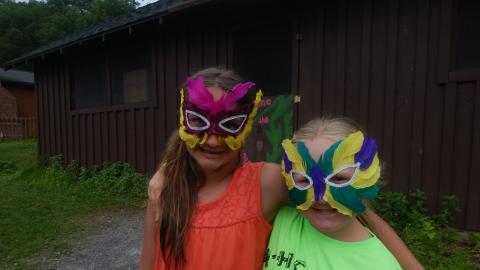 Two youth stand together with around each other wearing feathered masks.