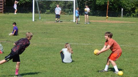 Camper using ball to block another ball being thrown at them in field. 